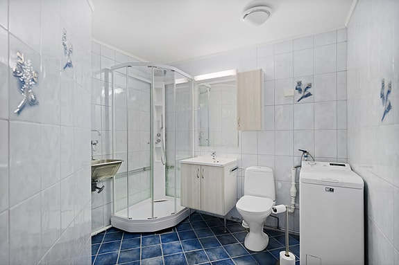 Flislagt bad utstyrt med dusjkabinett, servant med skap, toalett, opplegg for vaskemaskin, skyllekum og varme i gulv