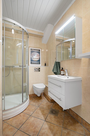 Pent baderom med dusjkabinett, vegghengt toalett og moderne baderomsinnredning med speilskap og belys