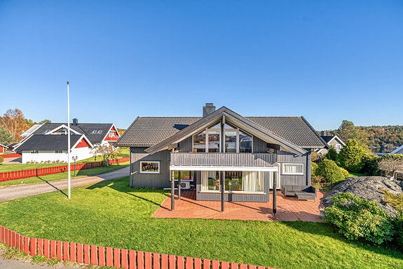 Eneboligens fasade mot hagen – grå kledning, store vinduer, plen og beplantning.