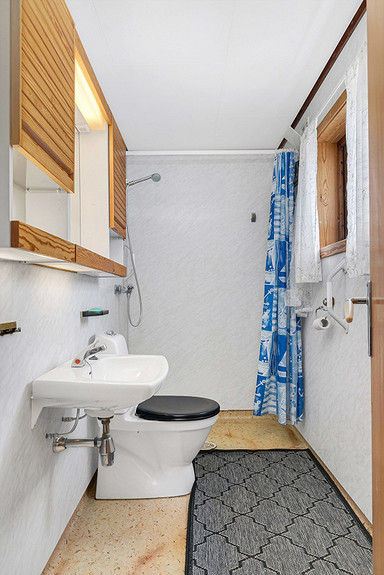 Badet har våtromsplater på vegger og våtromsbelegg på gulv. Her er dusjnisje og toalett.