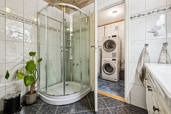 Moderne baderomsinnredning på badet og opplegg for vaskemaskin og tørketrommel i separat vaskerom.