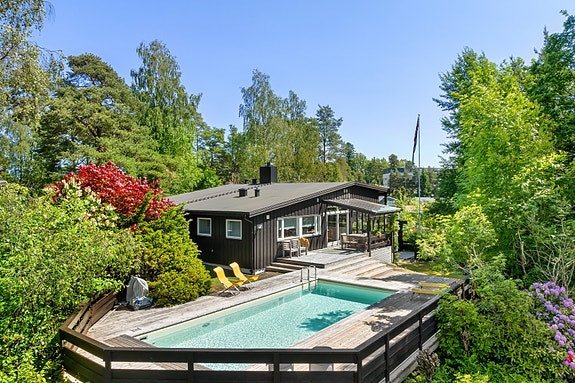 Velkommen til Strupeveien 30! Enebolig med basseng og stor terrasse, omgitt av frodig vegetasjon og trær.