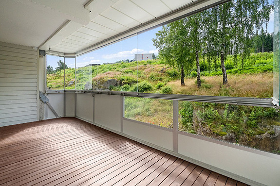 Romslig innglasset balkong med plass til en koselig sofagruppe samt spisebord og grill.