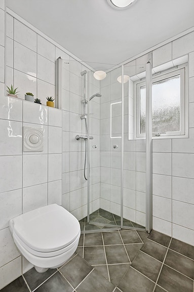 Nedsenket gulv i dusjnisje og vegghengt toalett.