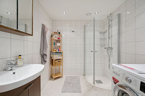 Delikat baderom med lyse fliser, moderne innredning og opplegg for vaskemaskin.