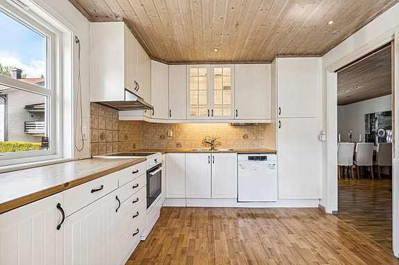 Stilrent og moderne kjøkken med hvitevarer og store vinduer som gir rikelig med dagslys.
