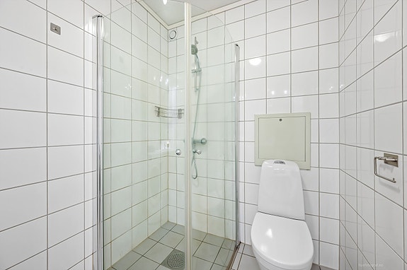 Pent flislagt bad med innredning bestående av klosett, dusjhjørne og baderomsinnredning med speilskap.