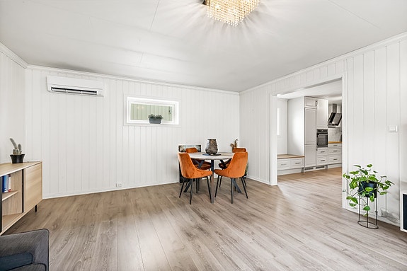 Moderne og lys stue med elegant laminatgulv, diskret klimaanlegg, og utgang til integrert kjøkkenløsning.