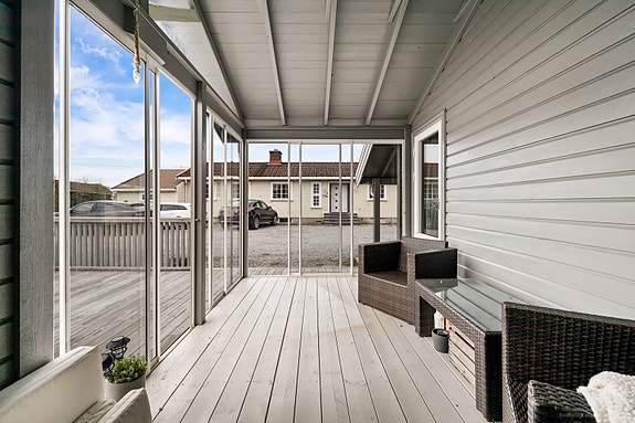 Lys og innbydende overbygd terrasse med moderne sittegruppe og utsikt mot rolig og solrikt gårdsplass.