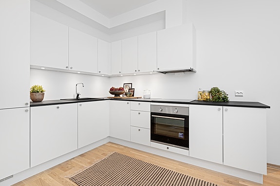 Utleiemegler Sør har gleden av å presentere en moderne og sentral leilighet på Lund! Kjøkkenet er stilrent med hvit overflate og belysning over benkeplaten.