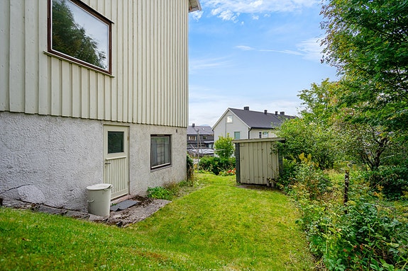 Hage på siden av huset med egen inngang til kjelleretasjen og utebod