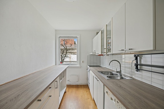 Lyst kjøkken med hvite glatte fronter og hvitevarer. Her er det godt med benkeplass.