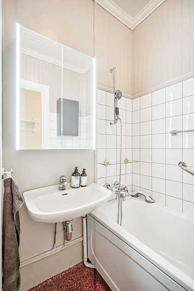 Badet er utstyrt med vegghengt servant med speilskap, badekar og gulvmontert toalett.