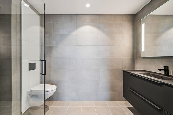 Vegghengt toalett og elegant servant med speil og belysning.