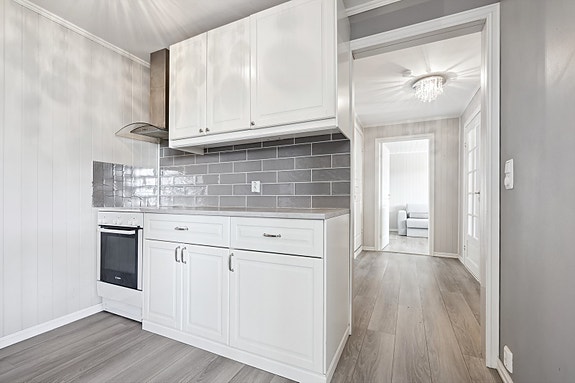 Pent kjøkken med profilerte fronter og fliser over benk