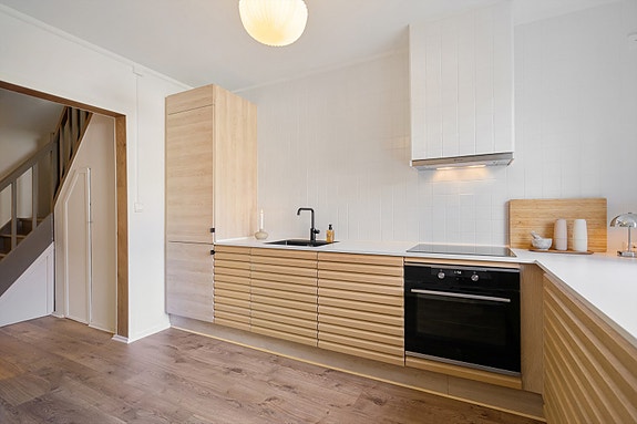 Tidløs og moderne kjøkken i lys eik, hvite fliser på veggen som rammer inn viften på en moderne måte