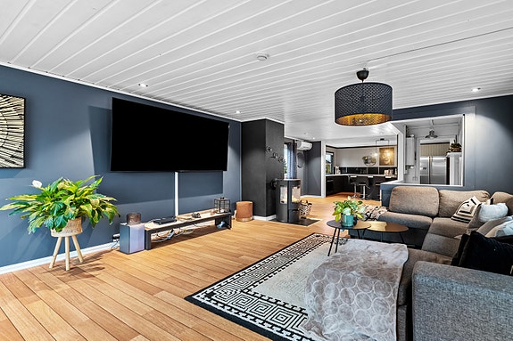 Stue med peis, utgang til hage. Lys og moderne atmosfære med parkettgulv og mørke vegger.