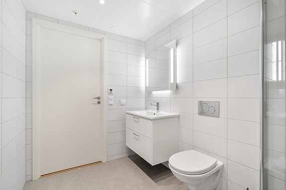 Badet leveres med hvit servant montert i benkeplate med underskap, samt speil med integrert lysarmatur over vasken for et praktisk og elegant preg.