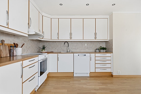 Laminert benkeplate med nedfelt oppvaskkum i stål, flisfelt over benk, Bosch oppvaskmaskin og Flexit ventilator i overskap. Det er også montert komfyrvakt.