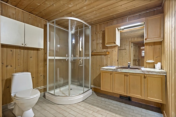 Bad i kjeller har dusjkabinett, toalett og servant med både over og underskap.  Vegger av panel, flislagt gulv med elektriske varmekabler.