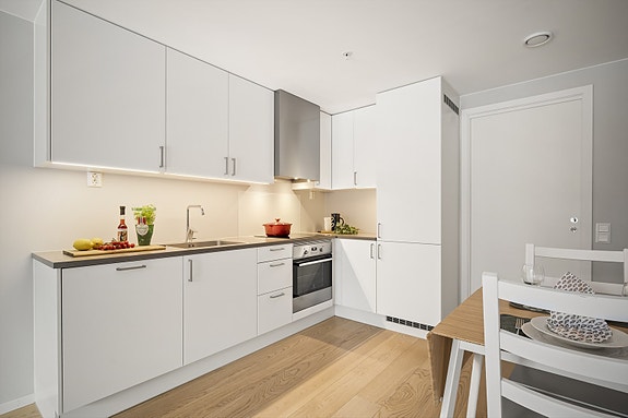 Vegg over kjøkkenbenk med glassplate ved platetopp og malte flater, samt. frittstående hvitevarer.