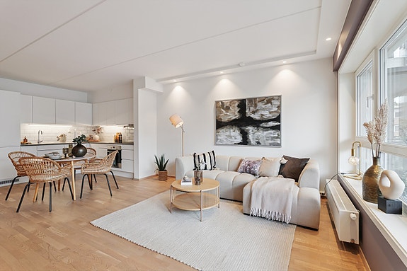 Stue med god plass til stor sofagruppe og spisebord mot kjøkken.