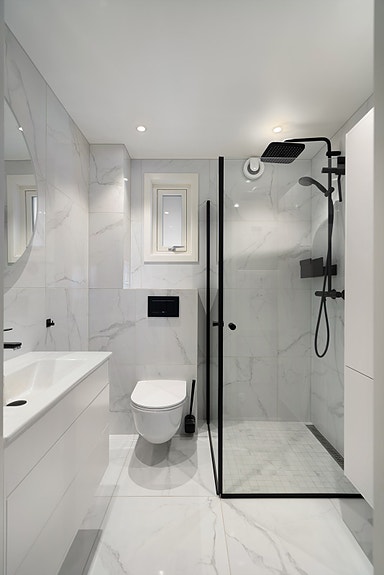 Moderne flislagt bad med heldekkende servant med oppbevaring, speil, vegghengt toalett, dusjvegger