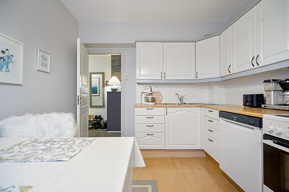 Kjøkkenet har lyse profilerte fronter med benkeplate av laminat, kjøl/frys, oppvaskmaskin og komfyr.