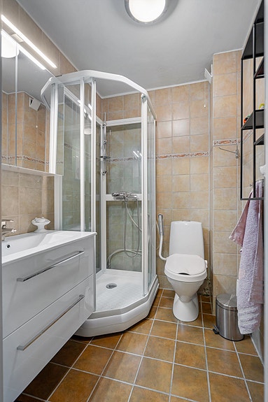 Flislagt bad med elektriske varmekabler i gulv, innredning med speilskap, heldekkende servant med oppbevaring, toalett og dusjkabinett.