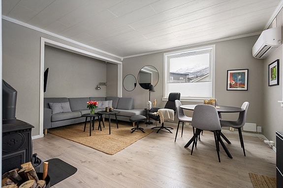 Stue har gulv av laminat, vedfyring og flere lysinnslipp som gir leiligheten en lys og luftig atmosfære.