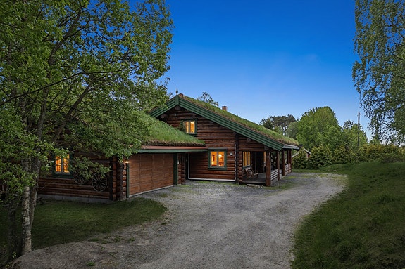 En solid tømmervilla fra 2000 med torvtak og en frittstående dobbelgarasje i samme stil. Garasjen har innlagt strøm og elbillader.