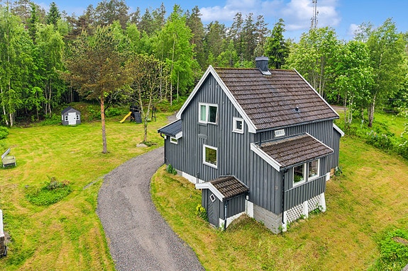 Eiendommen har en gruset innkjøring, parkeringsplass og skjermet hage mot skogkanten.