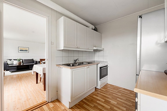 Praktisk kjøkken med profilerte fronter, laminatbenkeplate, flislagt vegg og dobbel oppvaskkum i rustfritt stål.