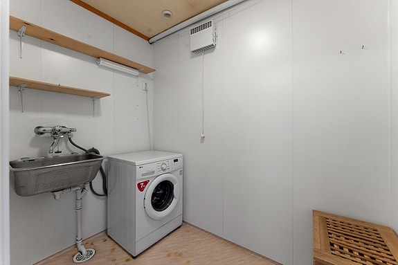 Praktisk vaskerom med opplegg for vaskemaskin, skyllekar og veggmonterte hyller som gir gode oppbevaringsmuligheter.