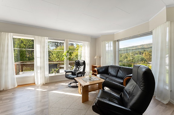 Innbydende sitteavdeling med sofa og stoler, hvor panoramautsikten virkelig kommer til sin rett. Fra stue er det direkte adkomst til terrasse.
