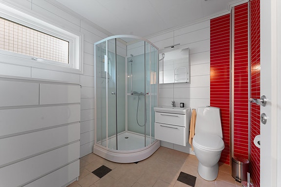 Lyst og praktisk bad med våtromsplater på veggene og flislagt gulv. Badet er innredet med dusjkabinett, toalett, servant med underskap og speilskap.