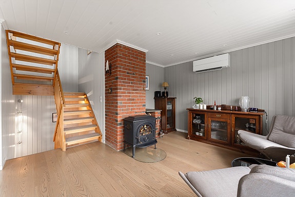 Romslig stue i 2. etasje med plass til møblering i flere soner. Peisen er plassert ved sittegruppen og gir varme og hygge på kalde dager.