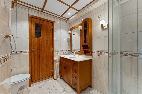 Stilrent bad med flislagte vegger og gulv med behagelige elektriske varmekabler. Badet er praktisk innredet med nedfelt servant, veggmontert toalett og dusjkabinett.