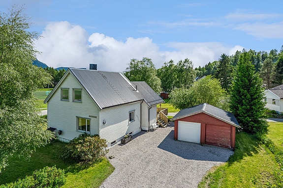 Romslig gårdsplass. Dobbeltgarasje. Hvit port med portåpner.