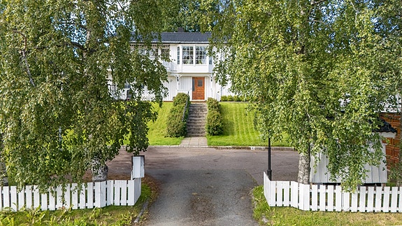 Innbydende adkomst med steinsatt trapp, velholdt hage innrammet av gjerde, frodig hage og bjørketrær.
