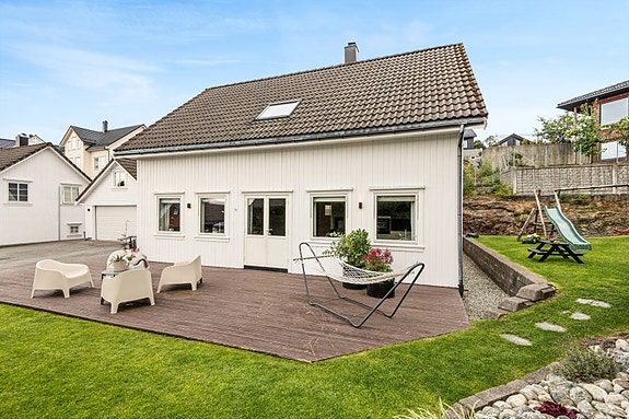 Pent anlagt hage med plen og en stor terrasseplatting.