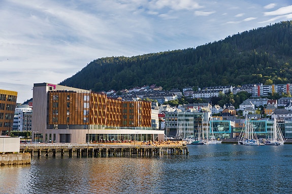 Moxy Bergen – Volum og fasade sett fra sjøsiden. Første etasje danner en markert sokkel som forankrer bygget på kaifronten.