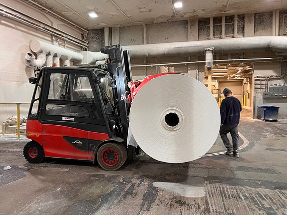 Vi bruker både klem-trucker og traverskraver for å håndtere de store papir-rullene.